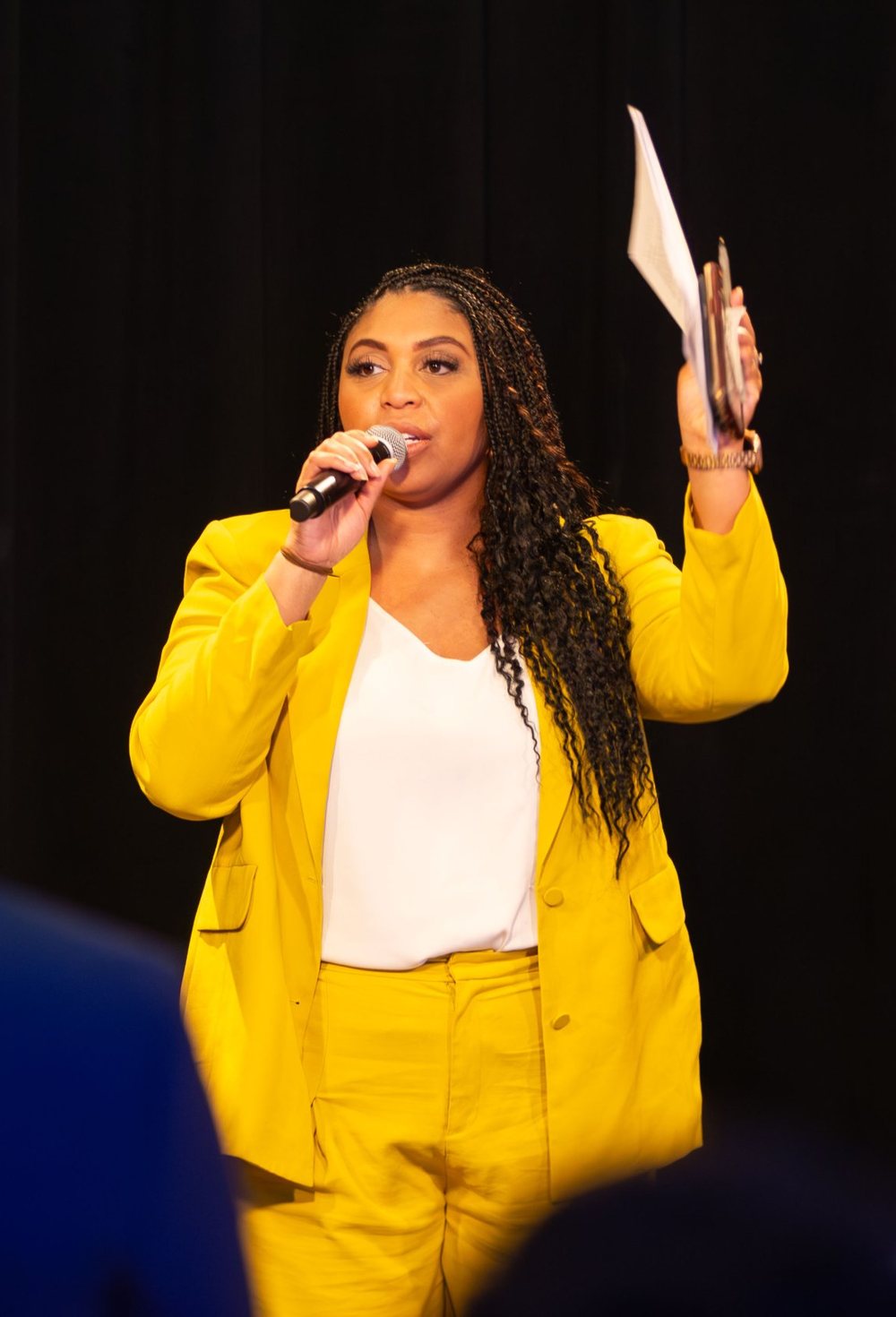 Alexis speaking on stage in a yellow suit